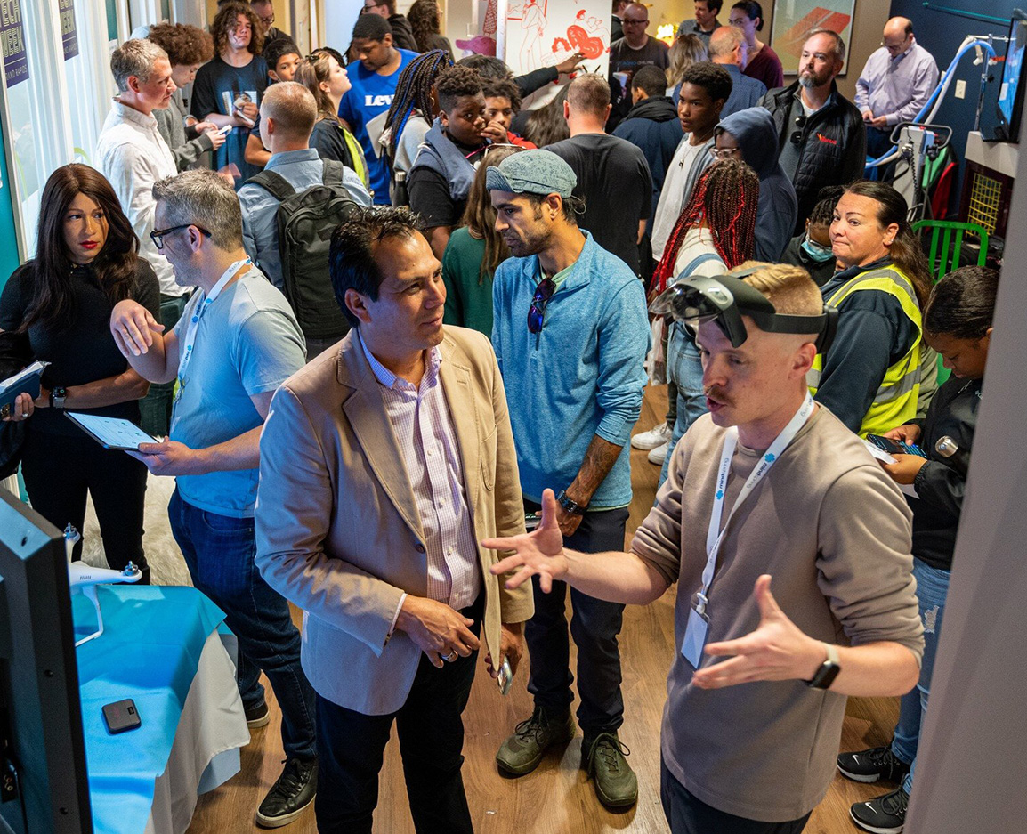 A man with a VR headset on, giving a demo to a crowd of people.